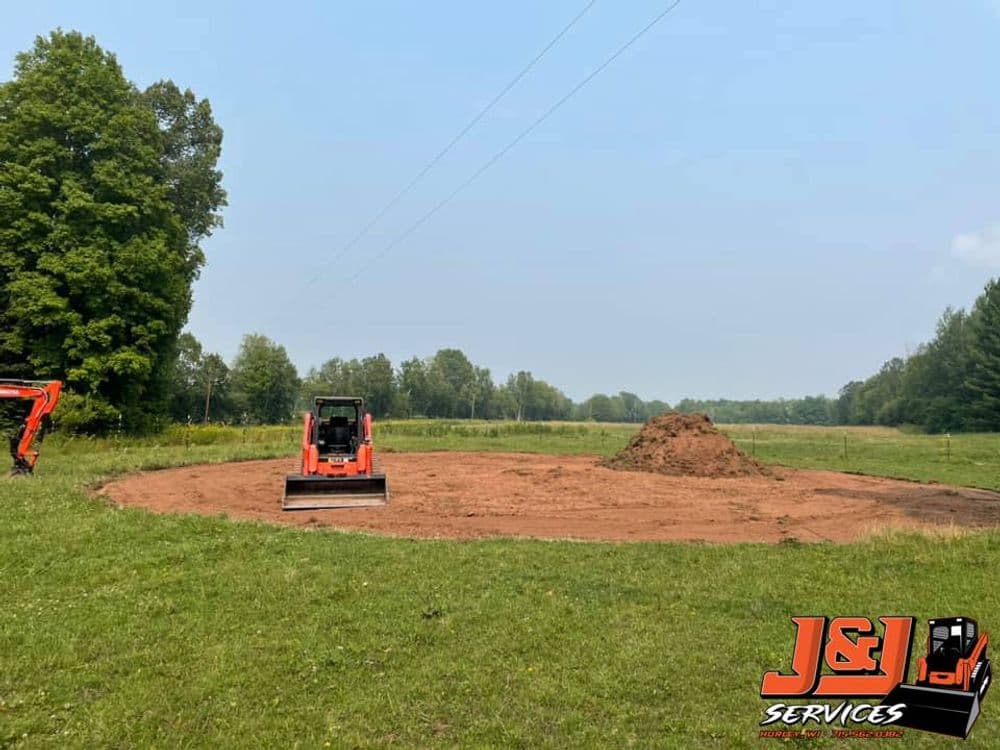 Excavator on a construction site preparing ground with a dirt pile in a grassy field.