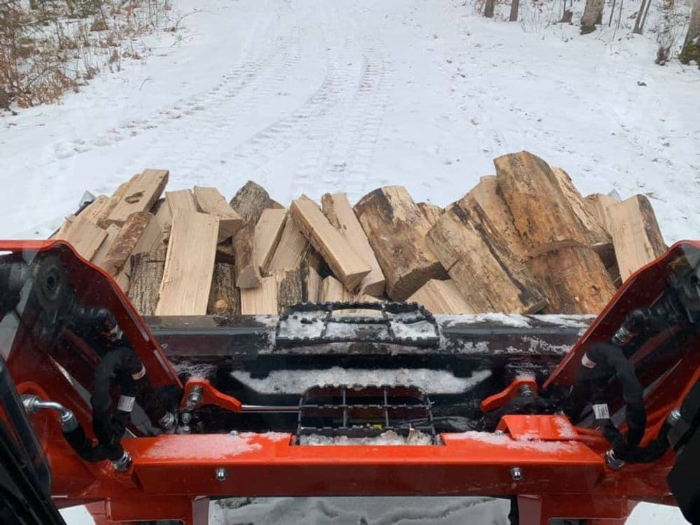 View of a snow-covered path with a tractor carrying a load of firewood.
