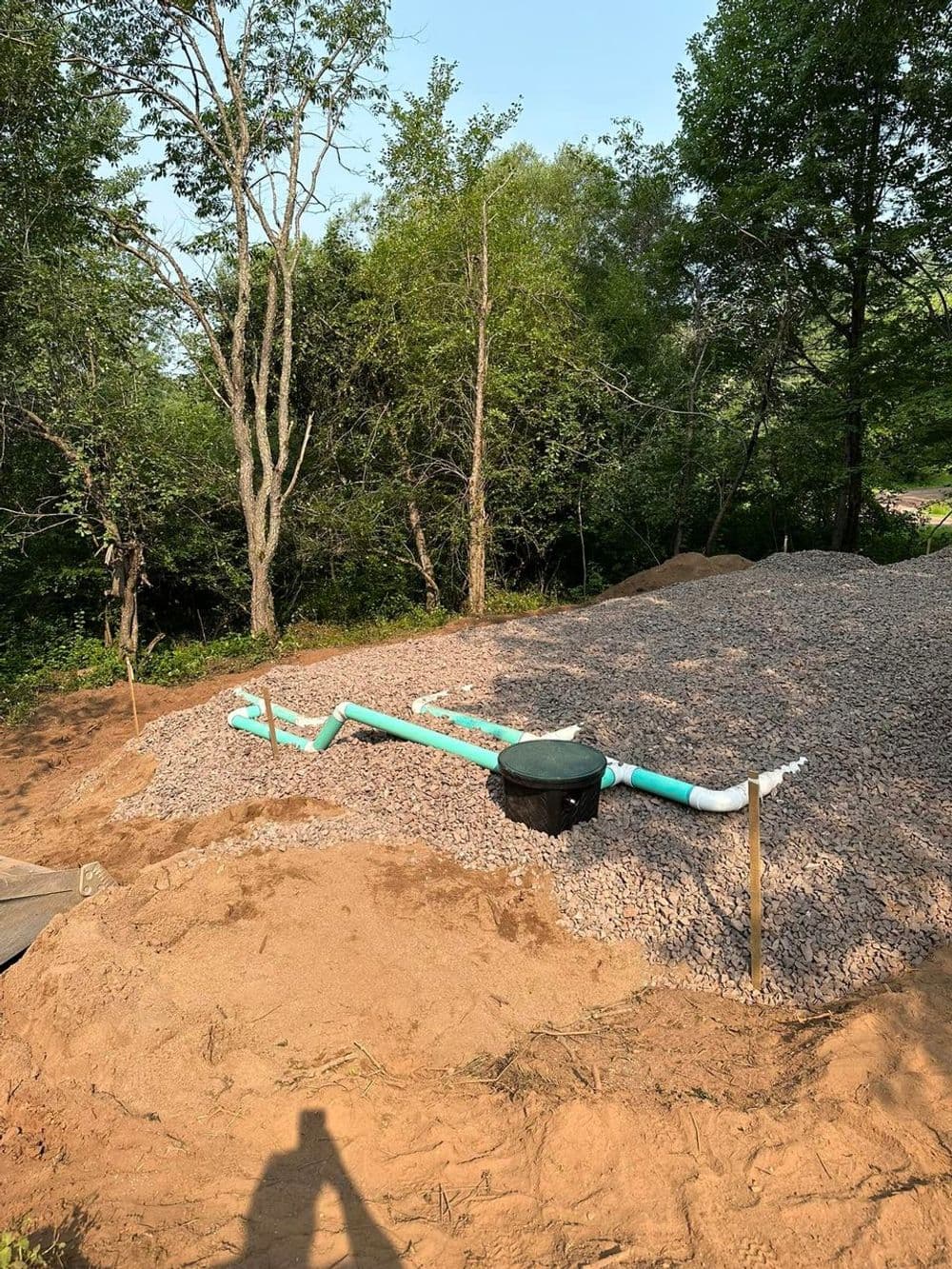 Newly installed drainage system with green pipes on gravel near wooded area.