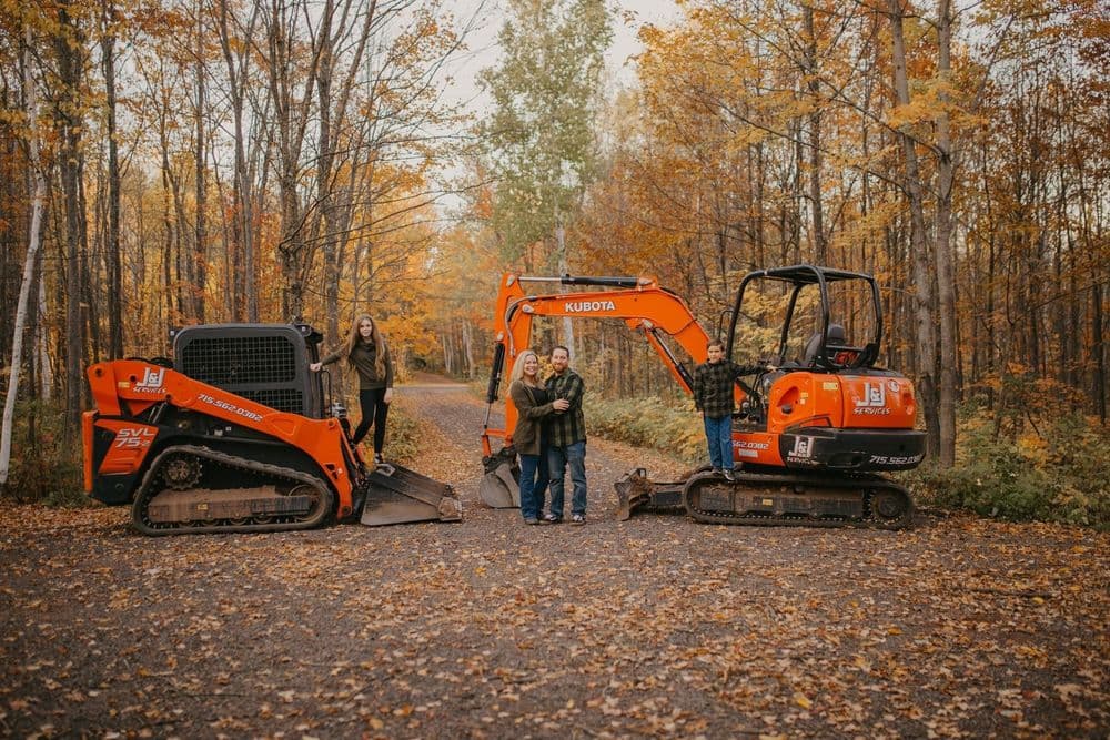 Couple standing between two orange construction vehicles on a forest trail in autumn.