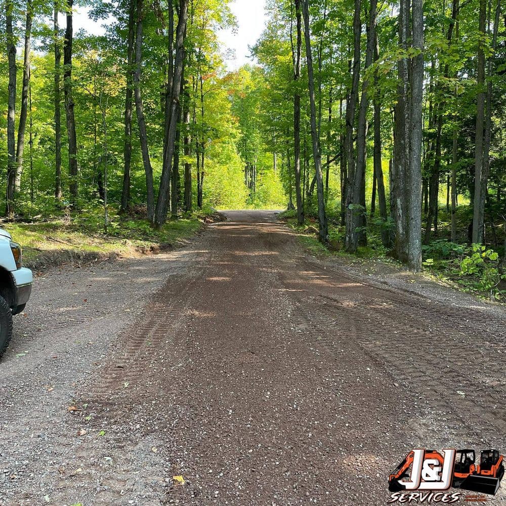 Gravel road surrounded by lush green trees, leading through a forest area.