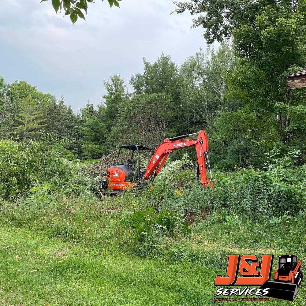 Excavator in a wooded area, clearing brush and debris for J&L Services.