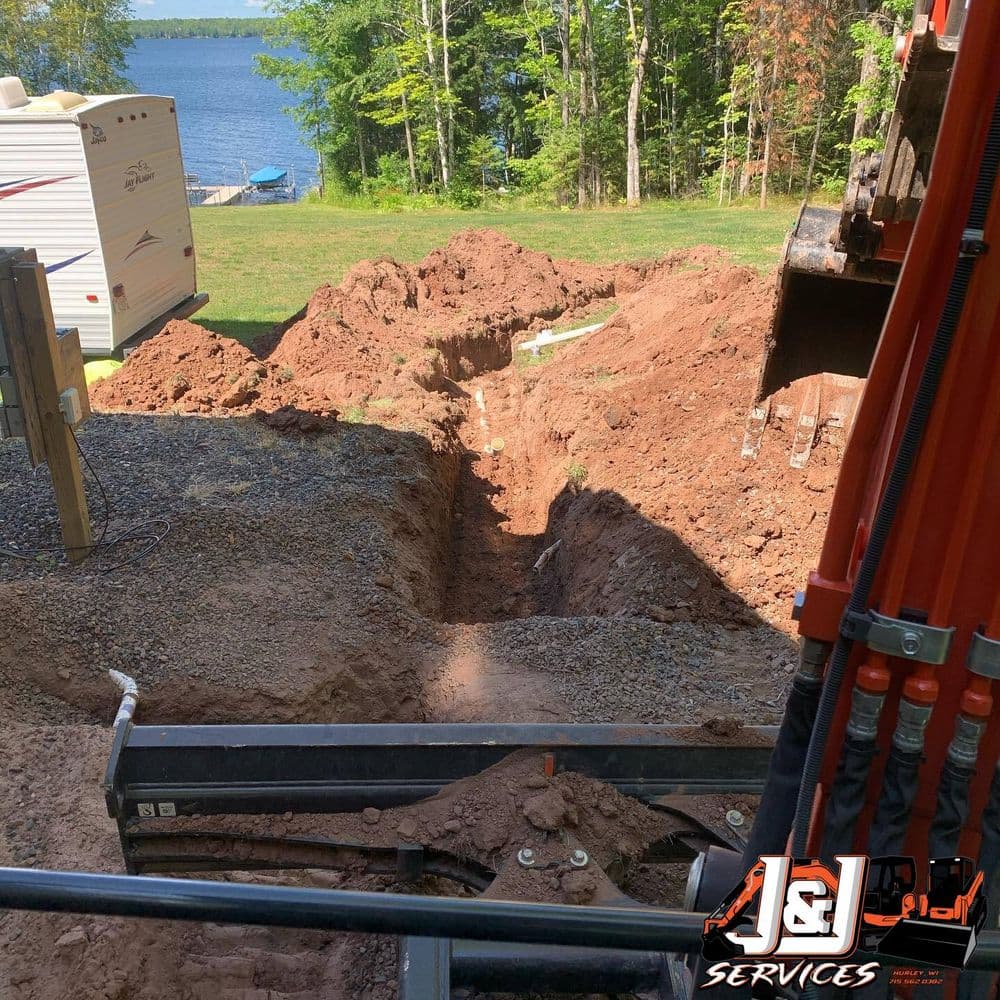 Excavation site with a deep trench near a lake, showing construction equipment and gravel.