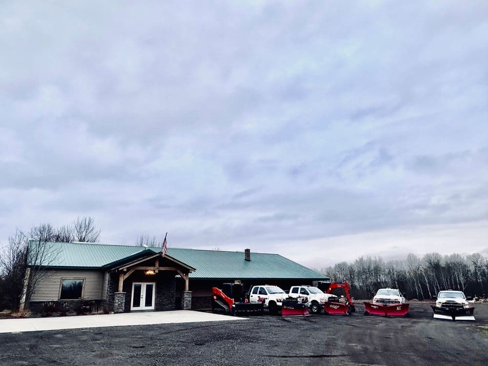 Exterior view of a building with snow plows and vehicles parked outside on a cloudy day.