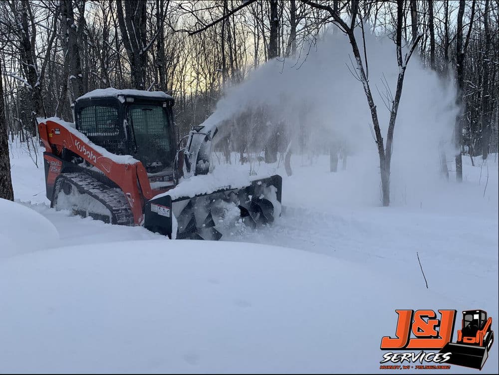 Snow removal with a skid steer loader in a winter forest setting at J&L Services.
