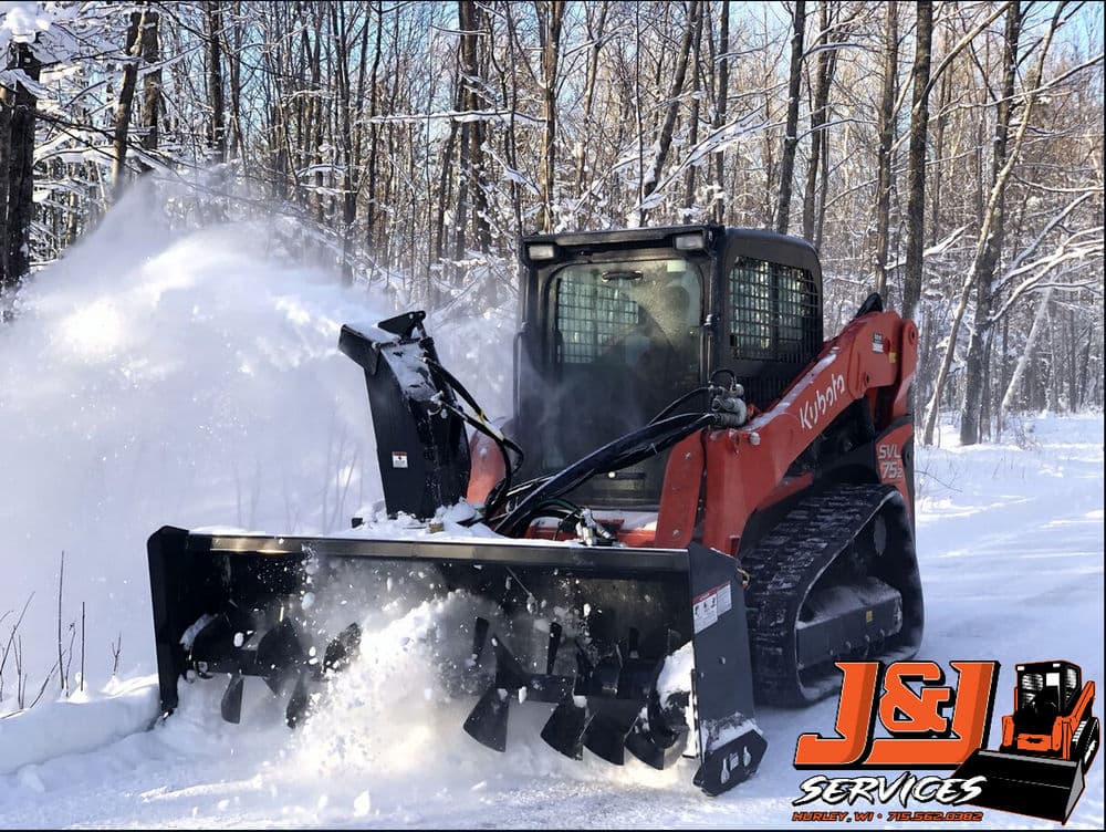 Snow plow clearing a path in a snowy forest, featuring J&L Services logo.