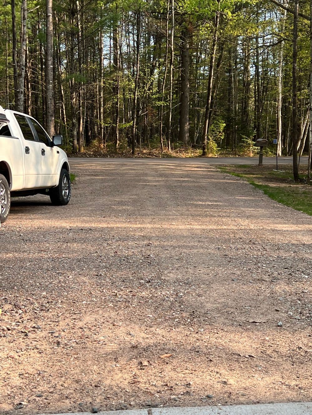 Gravel road in a wooded area with a white truck parked on the side.