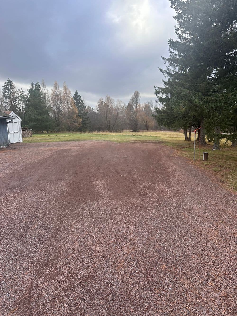Gravel lot surrounded by trees and cloudy sky, perfect for outdoor activities or parking.