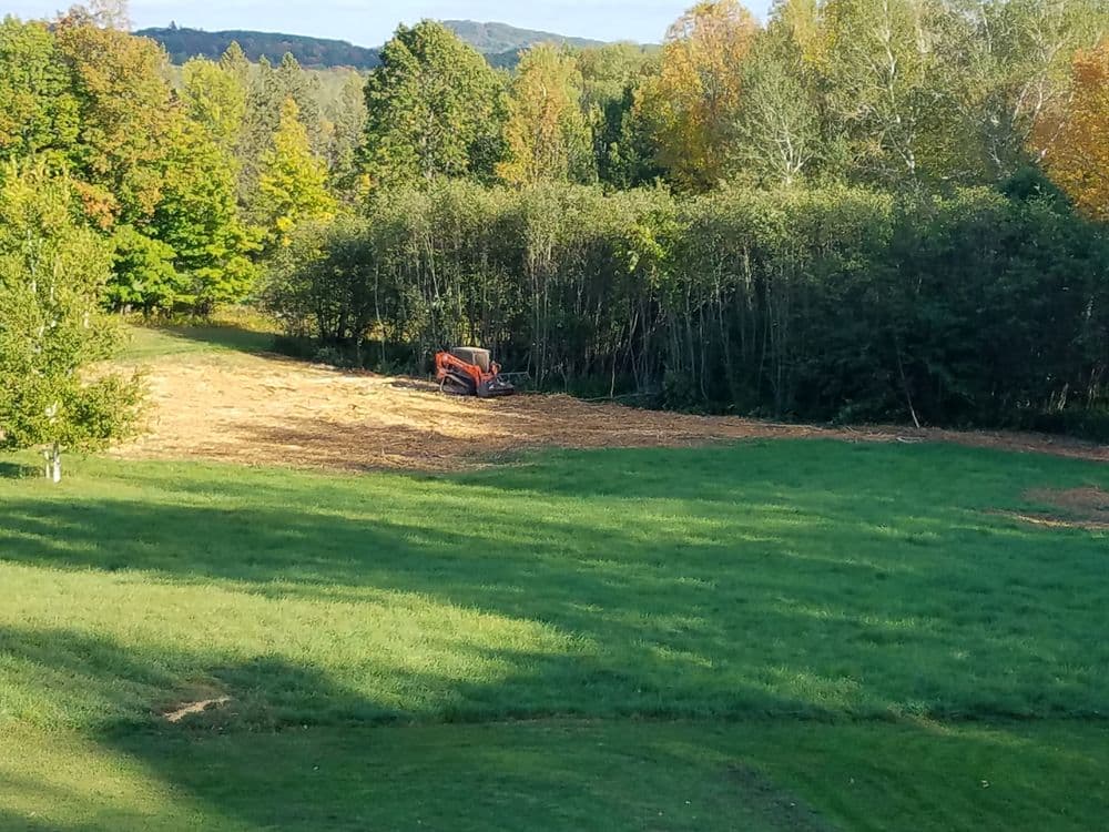 Tractor working in a field surrounded by trees and autumn-colored foliage.