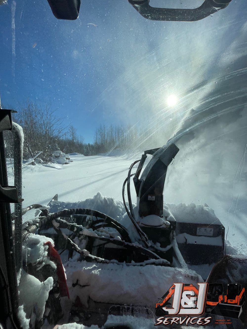 View from a snow plow cab clearing deep snow on a sunny winter day.