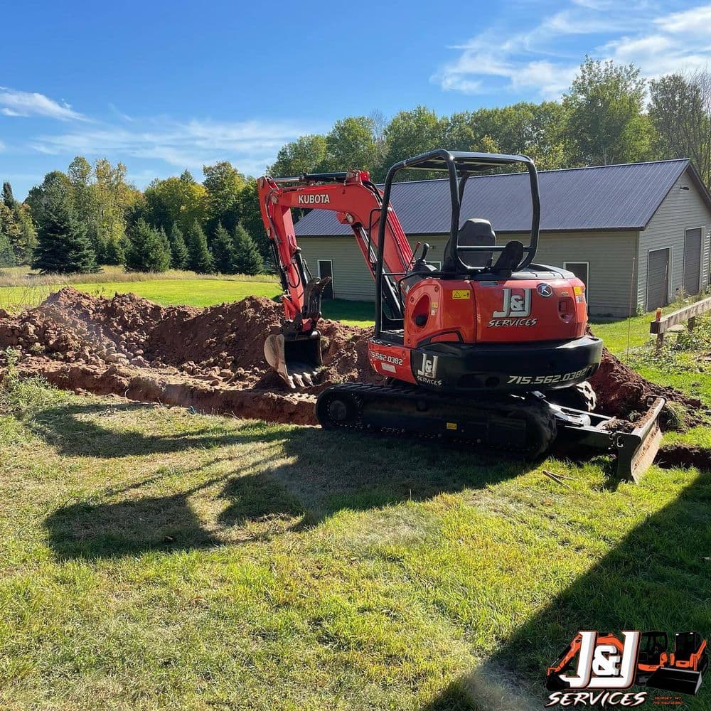 Excavator digging a trench on a residential property with a garage in the background.