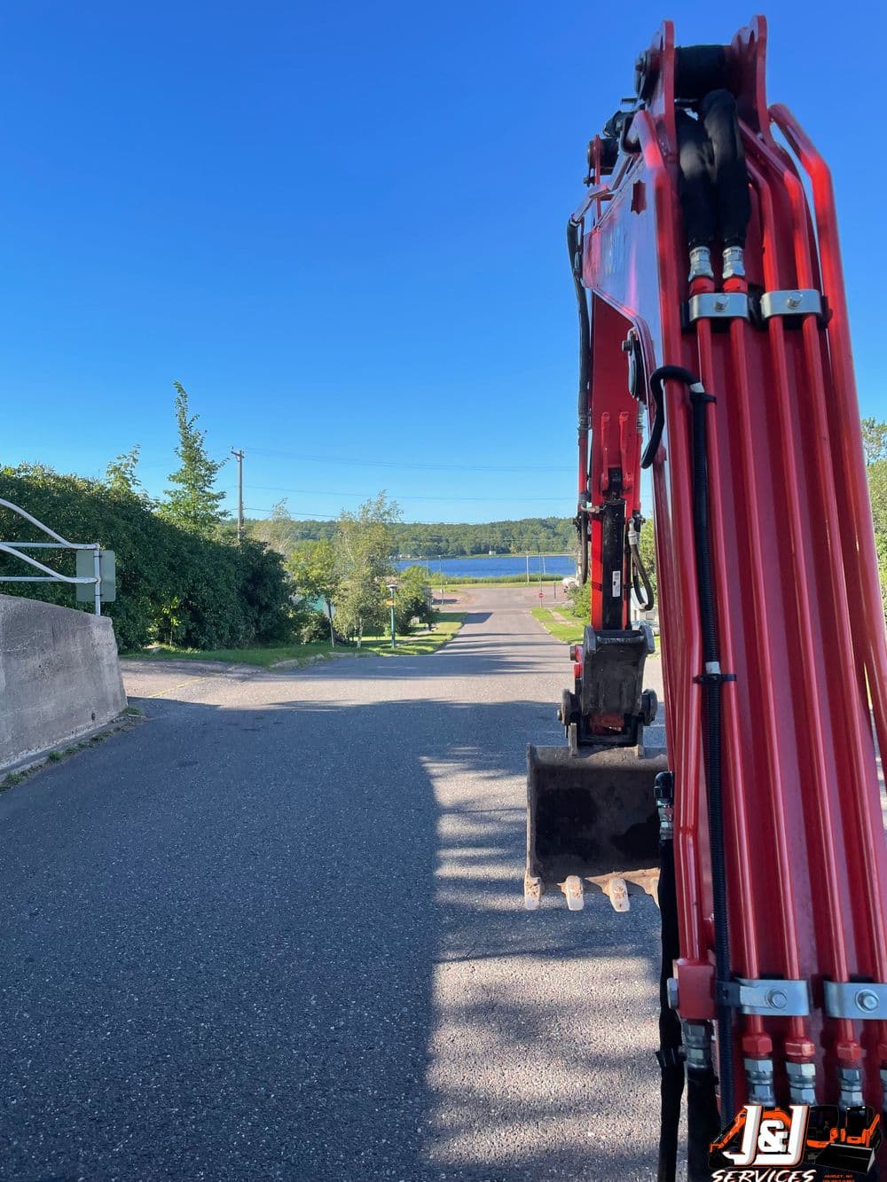 View from an excavator overlooking a road leading to a serene lake and greenery.