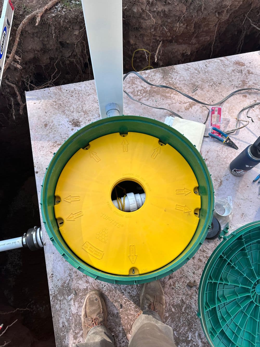 Yellow round access cover on a green septic tank with tools and equipment nearby.