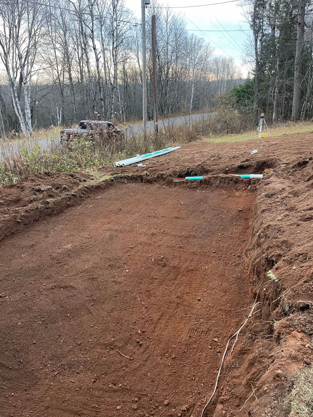 Excavated ground for construction with utility lines in rural area, trees in background.