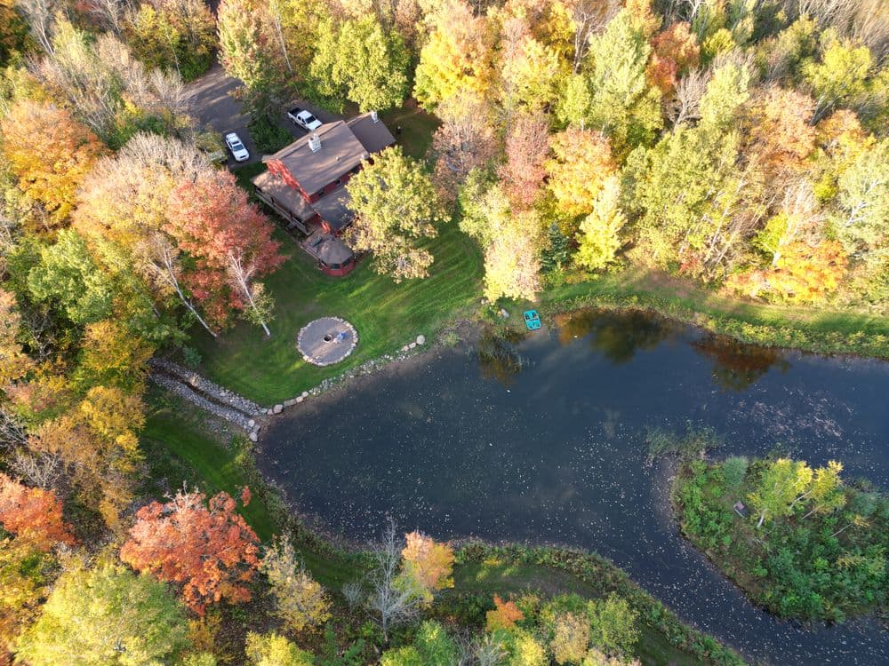 Aerial view of a house surrounded by vibrant autumn trees and a serene pond.