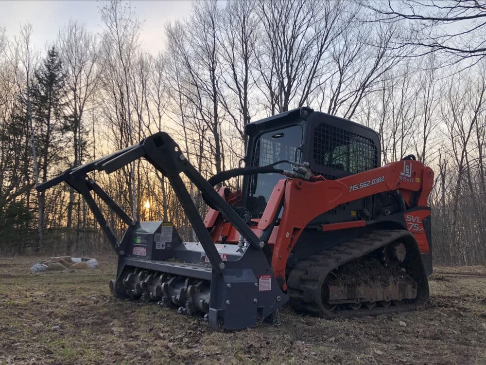 Bobcat skid steer with mulching attachment in forest at sunset.