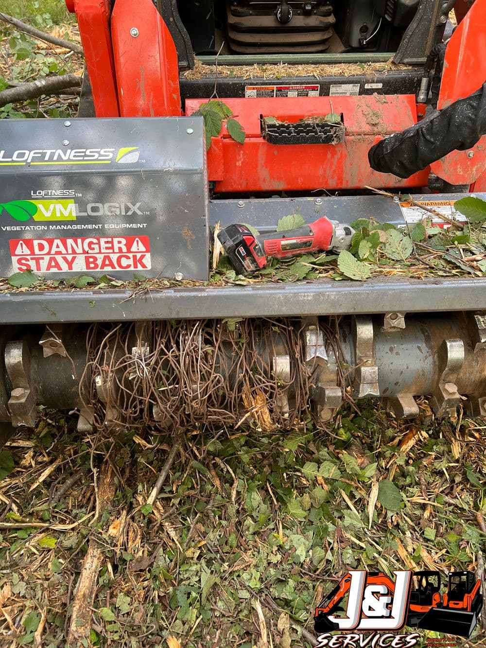 Vegetation management equipment covered in tangled roots and branches, warning sign visible.