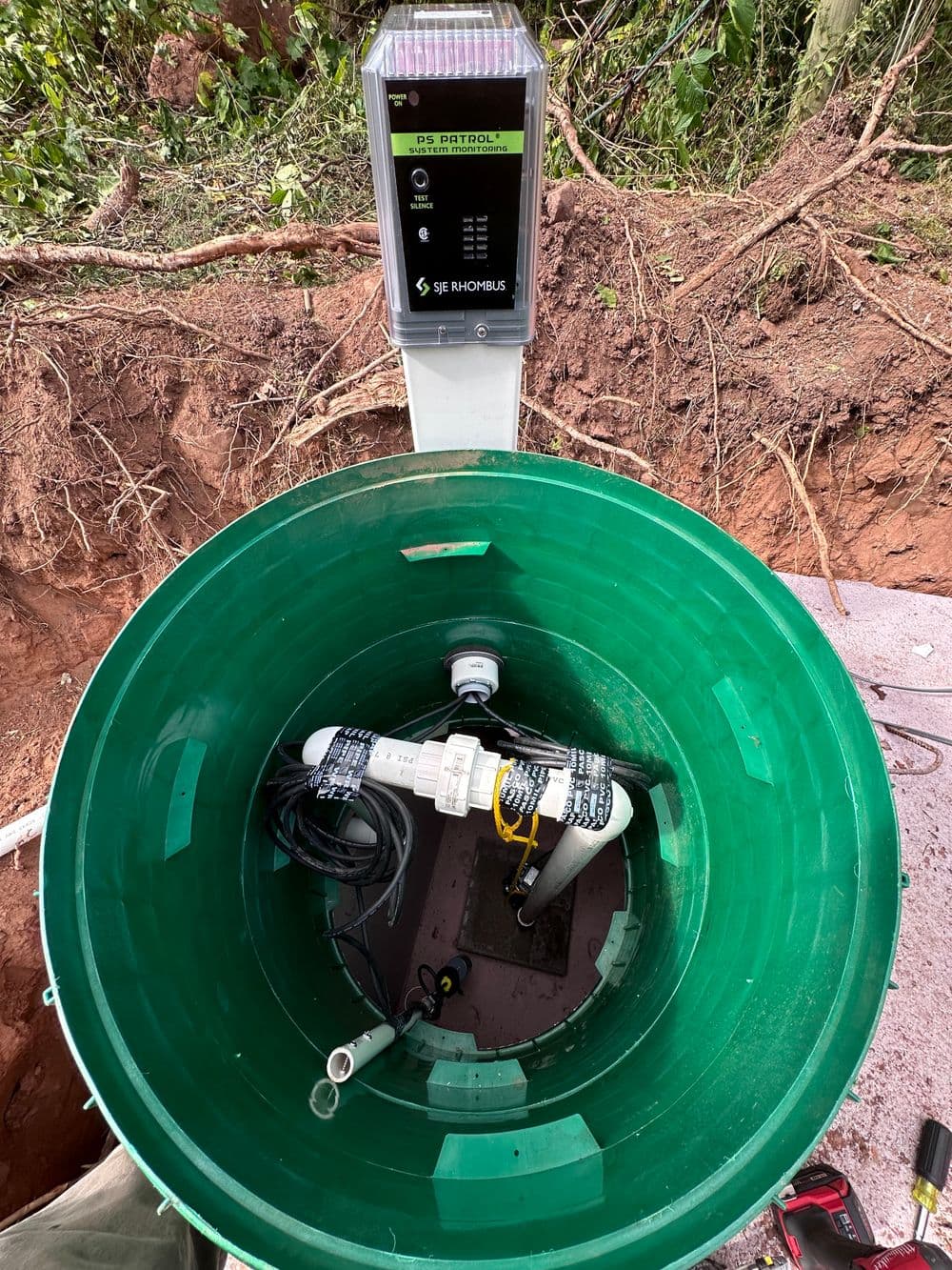 Green water tank with monitoring equipment inside and solar panel on top, set in a natural environment.