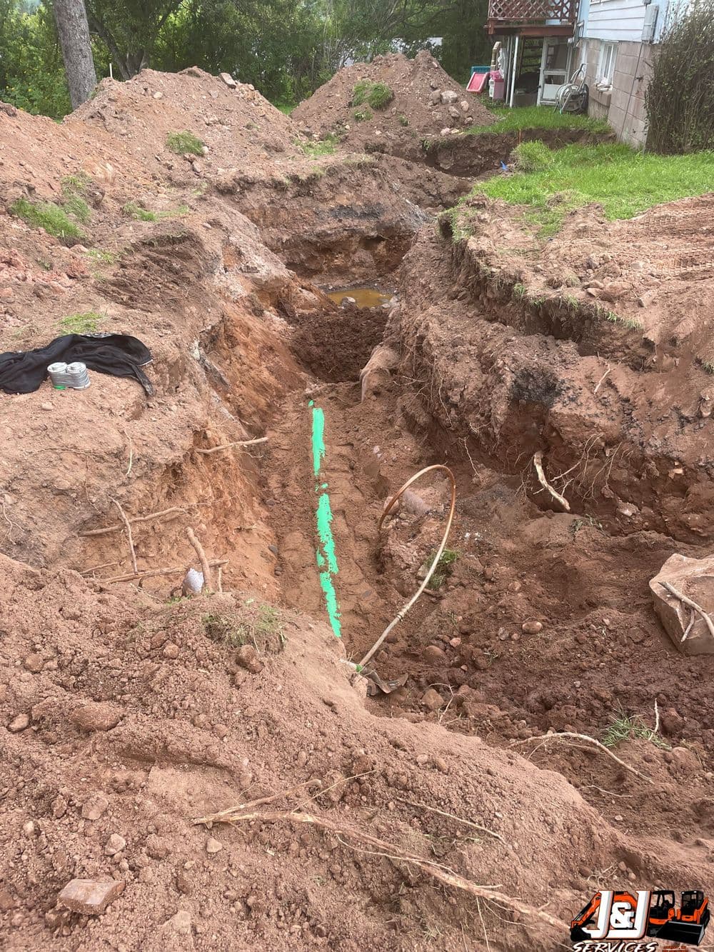 Trenched excavation for utility installation in a residential yard, showing dirt and pipes.