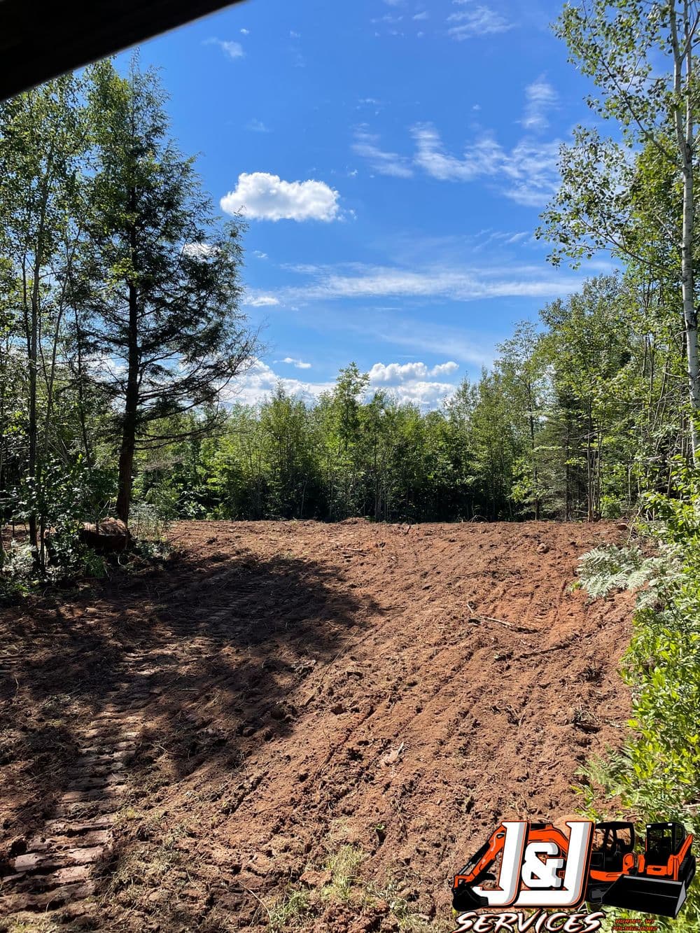 Cleared land with trees and blue sky, showcasing site preparation by J&L Services.