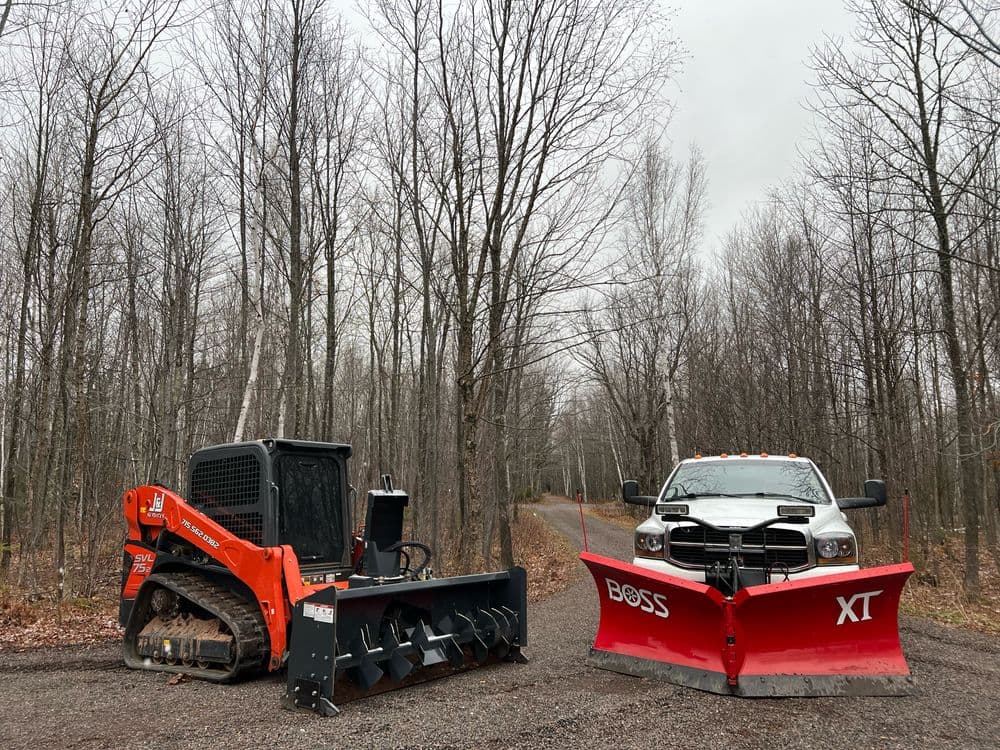 Bobcat snow removal equipment and truck with plow in wooded area during overcast weather.